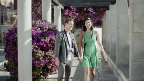 Front-view-of-young-couple-walking-along-blooming-alley.